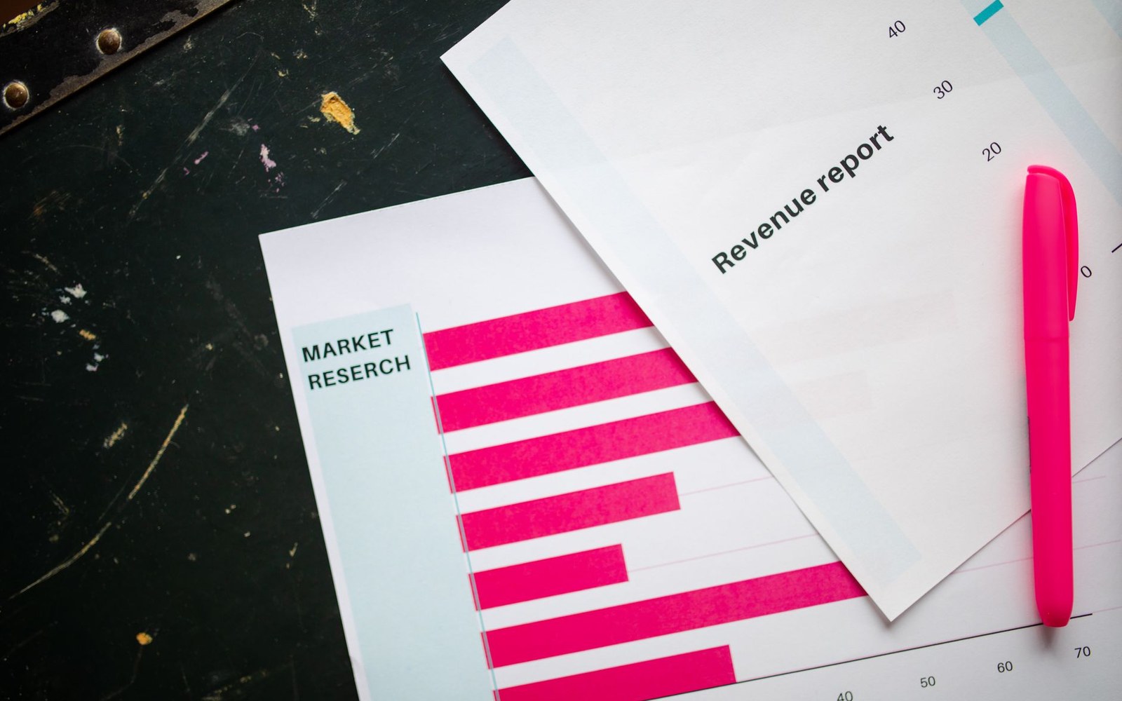 Market research bar chart and revenue report papers with a pink pen on a dark surface