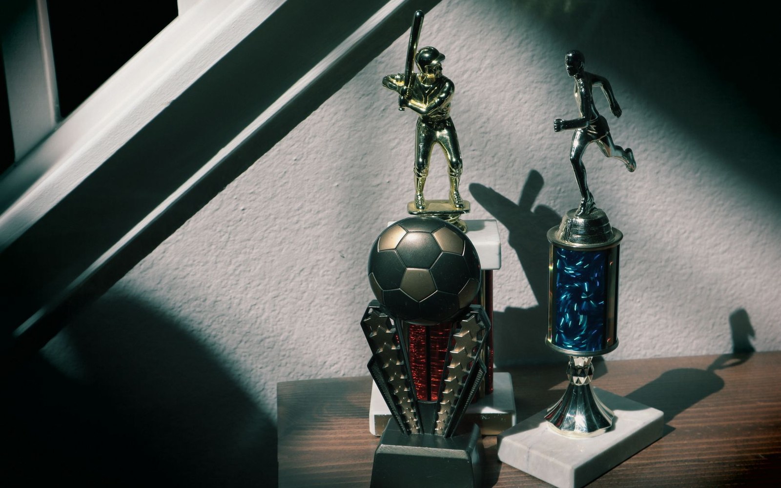 Two sports trophies with figurines of a batter and a runner sit on a shelf
