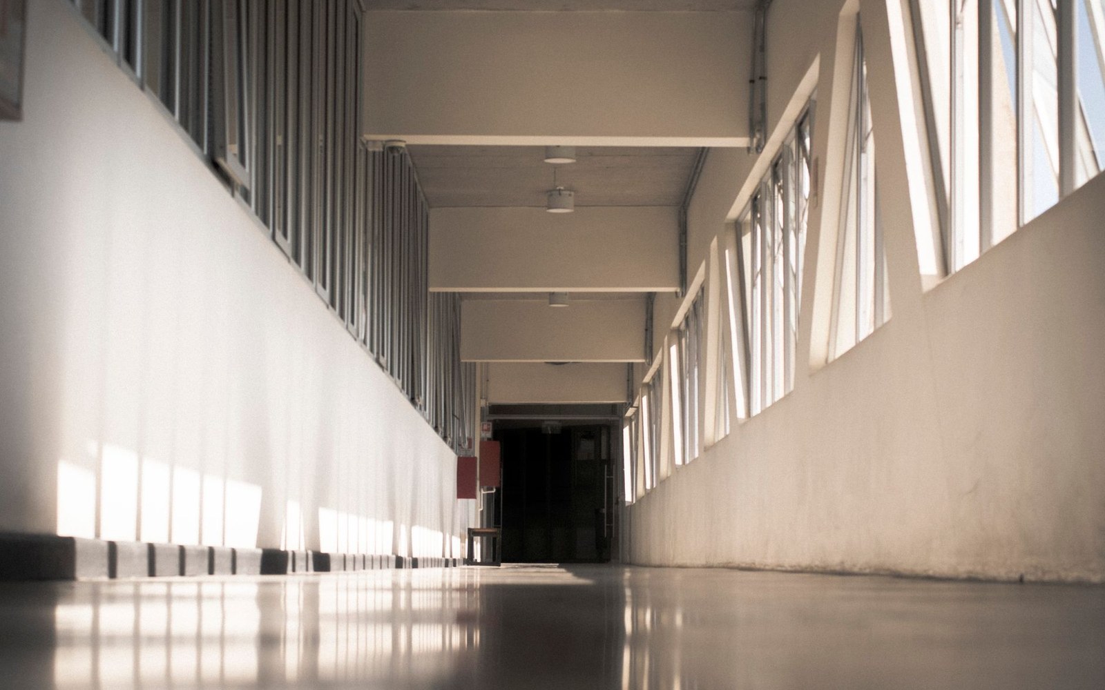 Long empty dormitory corridor with rows of windows casting striped light on the floor