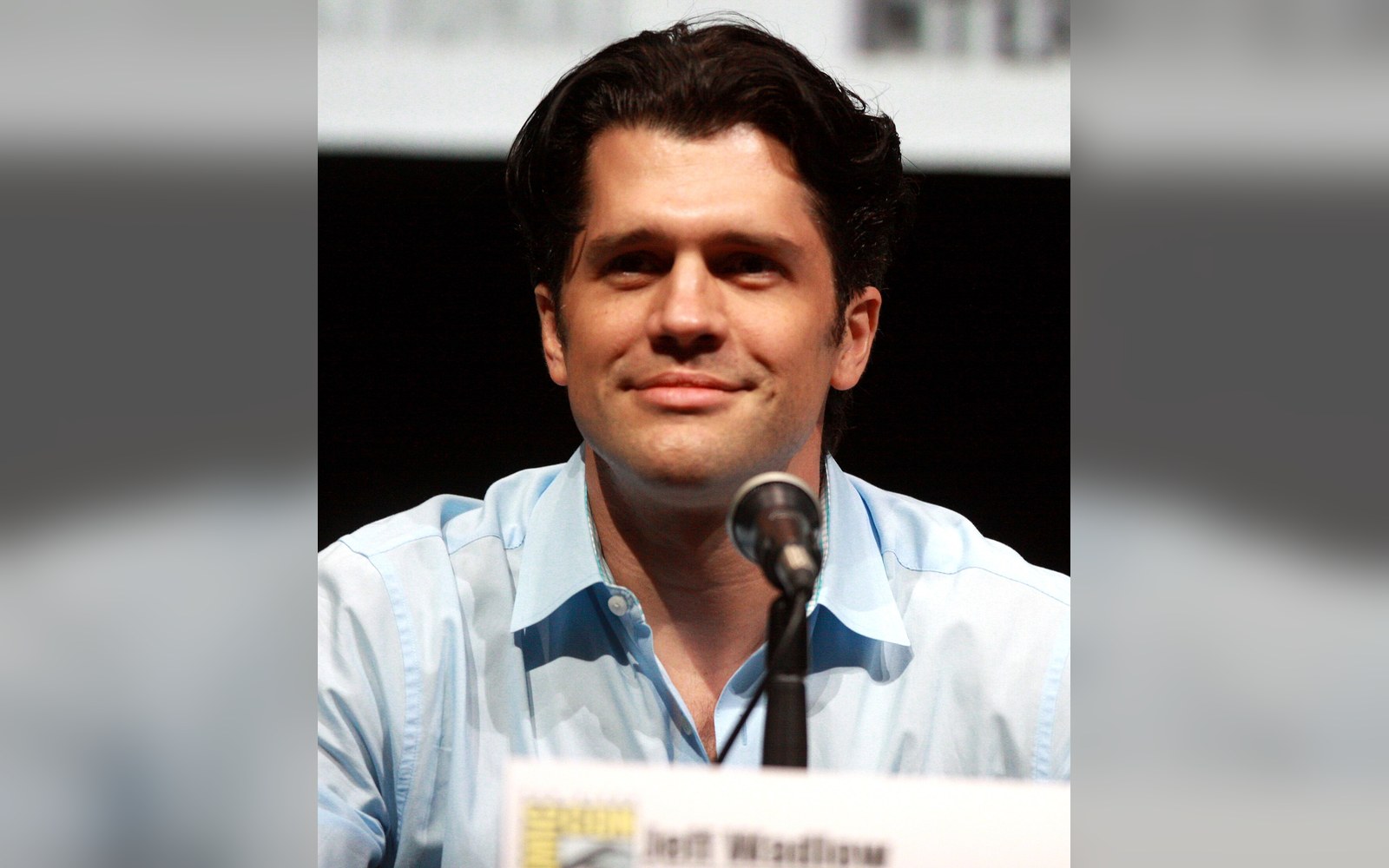 Man in a light blue shirt smiles behind a microphone at a panel discussion