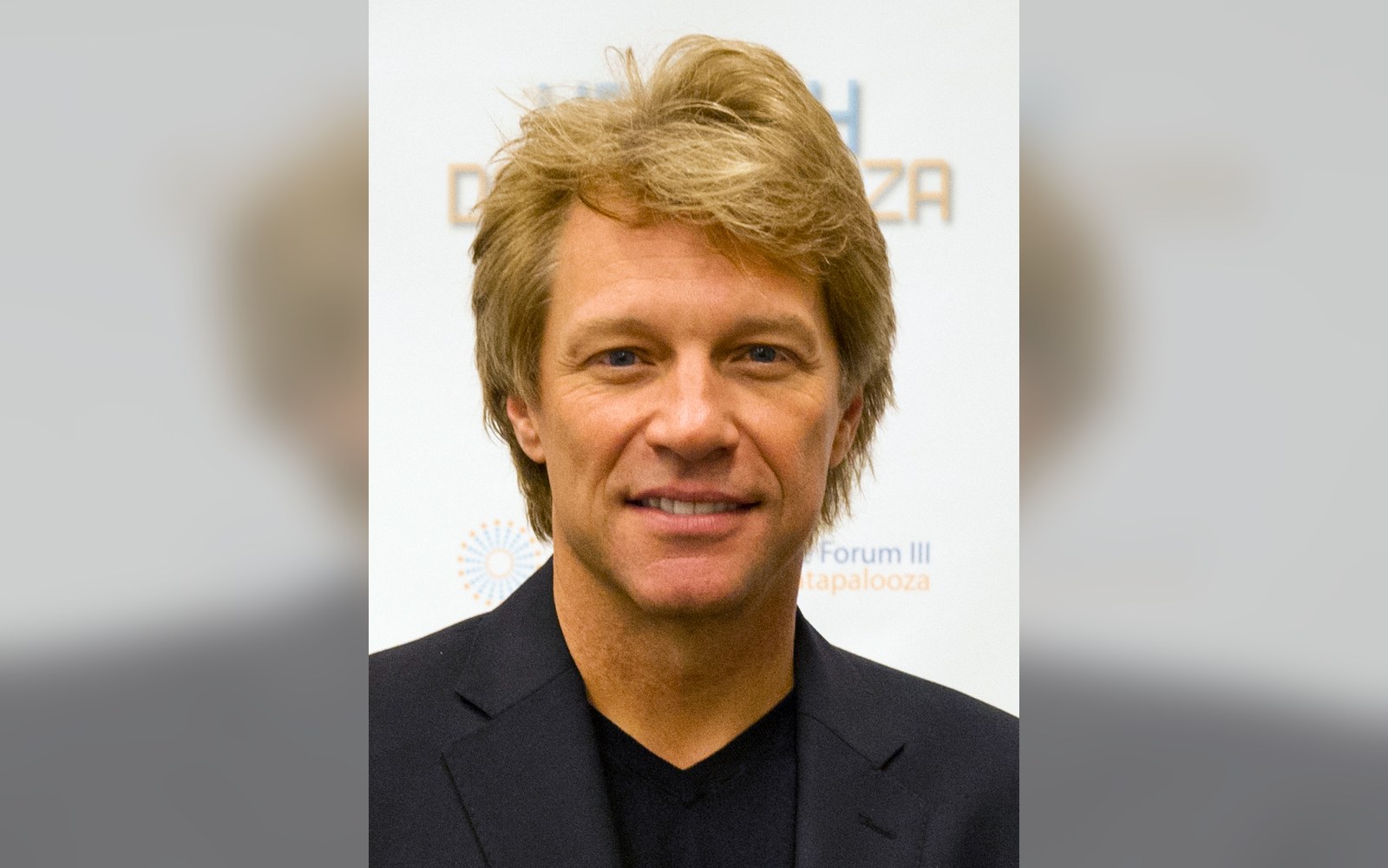 Jon Bon Jovi smiles in a black jacket at a media event