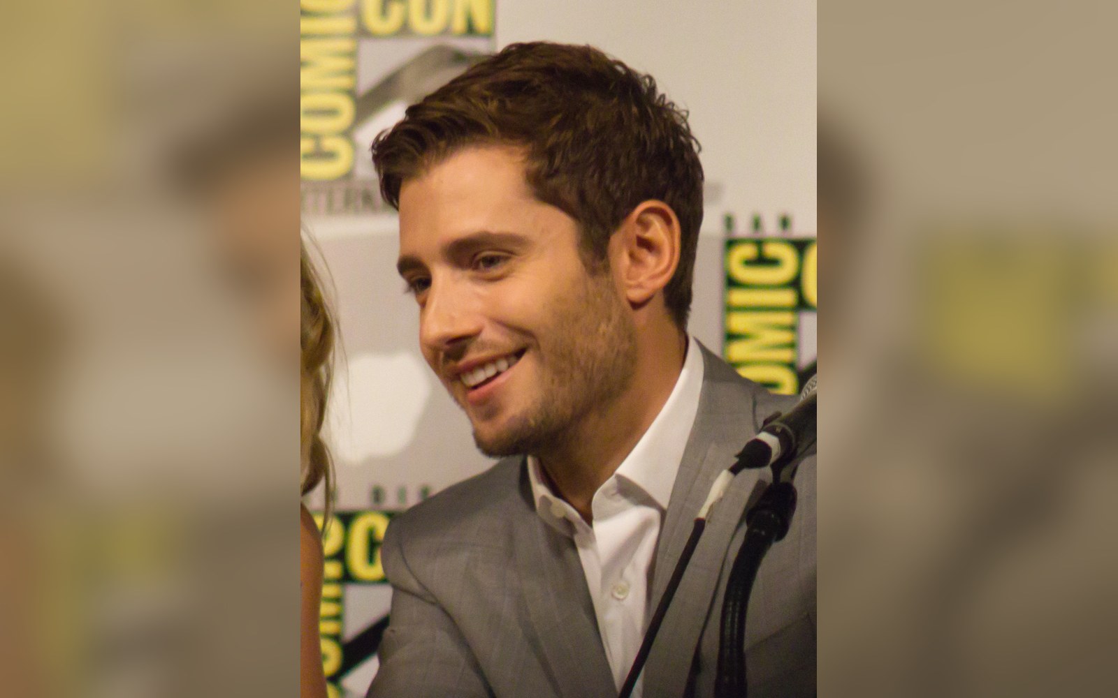 Man in gray suit smiling at a panel table with a Comic-Con backdrop