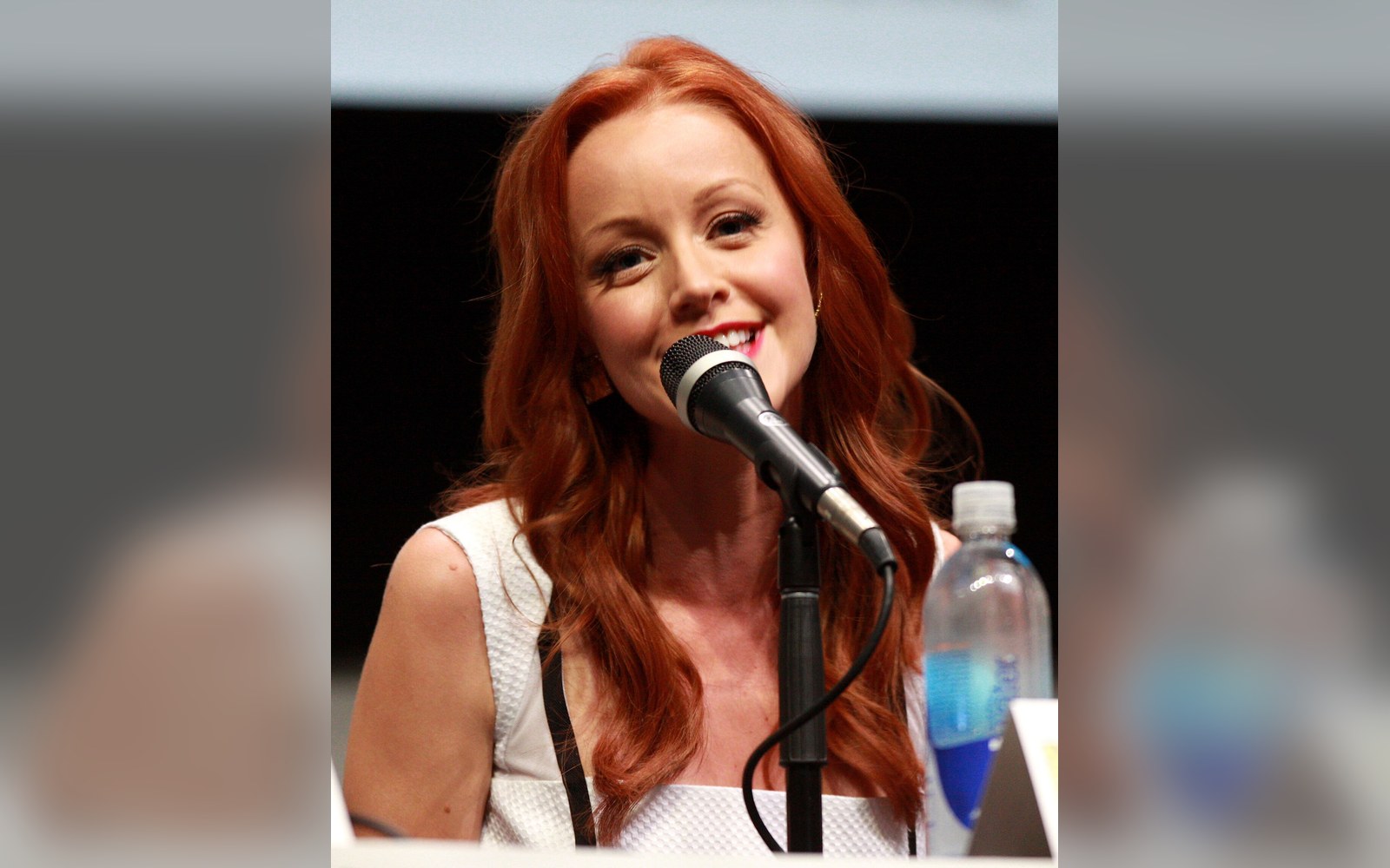 Red-haired woman smiling while speaking into a microphone at a panel discussion