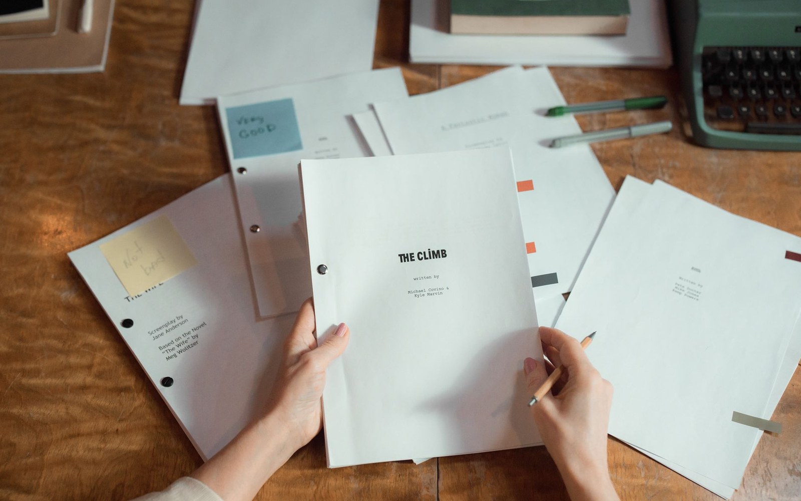 Hands hold a bound screenplay titled "The Climb" among scattered papers and a typewriter