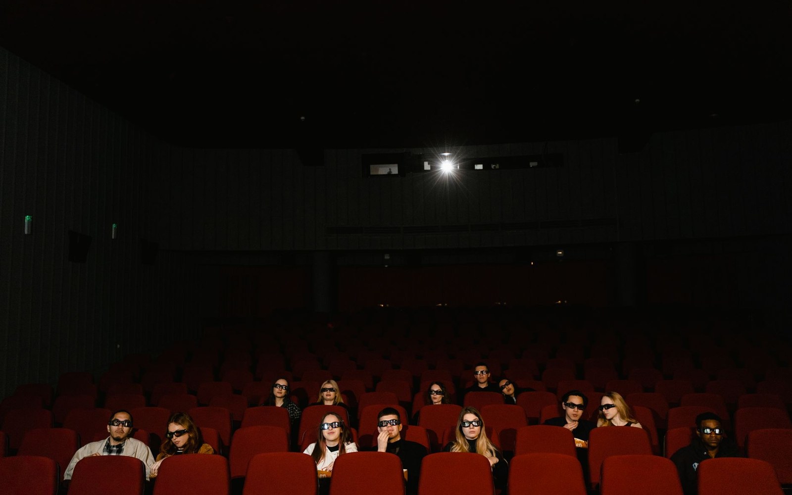 Adult figure silhouetted in a cinema auditorium, projector beam cutting the dark above them